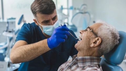 Yaşlı bir adam diş hekimi tarafından muayene ediliyor.