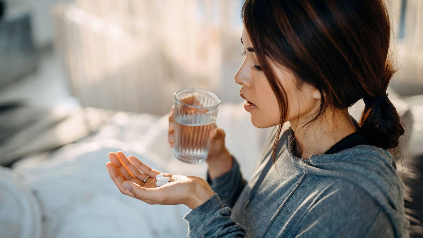 Antibiotic resistance (source: iStock/AsiaVision) A young woman is at home looking at some tablets on the palm of her left hand. Her right hand is holding a glass of water.