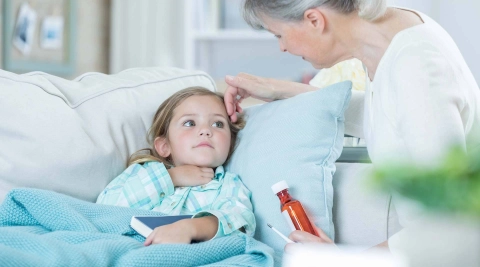 A young girl is feeling ill and is lying on the sofa, being cared for by her grandmother.