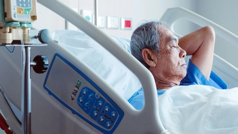 An elderly man lies on a hospital bed.