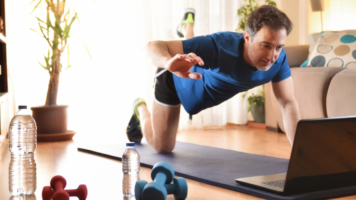 DiGA bei Erkrankungen des Bewegungsapparats (Quelle: iStock/Davizro) Ein Mann macht auf der Yogamatte Übungen vor seinem Laptop.