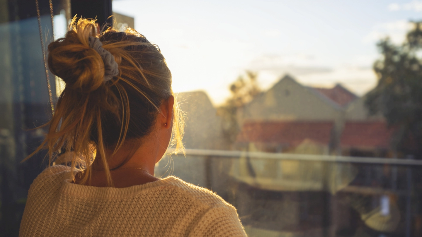 Unterstützung durch DiGA bei psychischen Erkrankungen (Quelle: iStock/courtneyk) Eine junge Frau schaut bei Sonnenuntergang durch das Fenster.