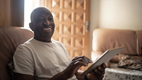 Улыбающийся человек сидит в кресле и пользуется планшетом.