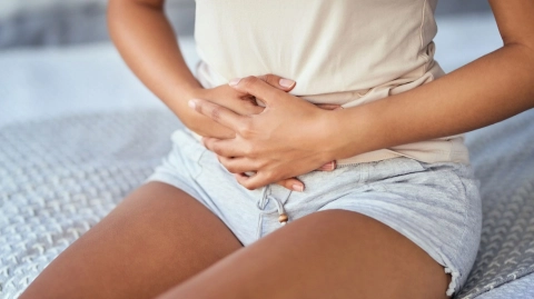 Endometriosis symptoms (source: Getty Images/LaylaBird) Lower abdominal pain: young woman sitting on a bed holding her abdomen with both hands.
