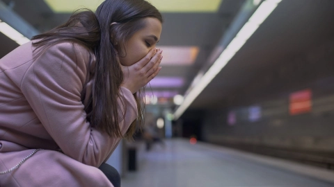 Bir kadın, gözleri kapalı halde bir metro durağında oturuyor.