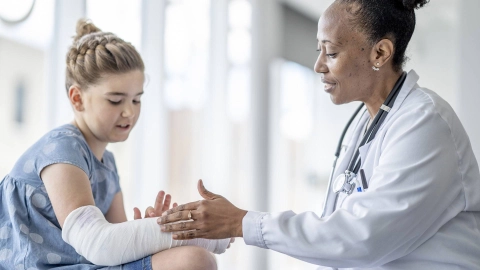 Bir doktor, bir kız çocuğunun alçılı kolunu muayene ediyor.