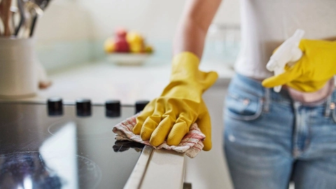 Человек в хозяйственных перчатках протирает плиту салфеткой.