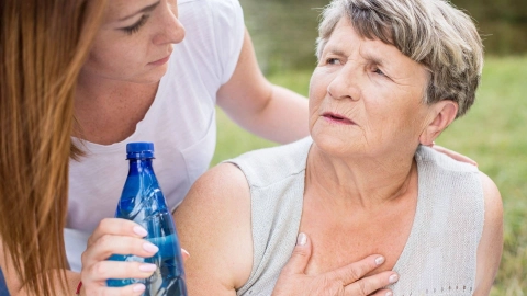 Older woman in a summer blouse with her hand on her chest. She is straining and turning round to a younger woman holding a bottle of water in her hand.