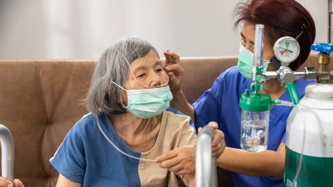 Bir bakıcı, evde ekstra oksijene ihtiyaç duyan bir kadına yardım ediyor.