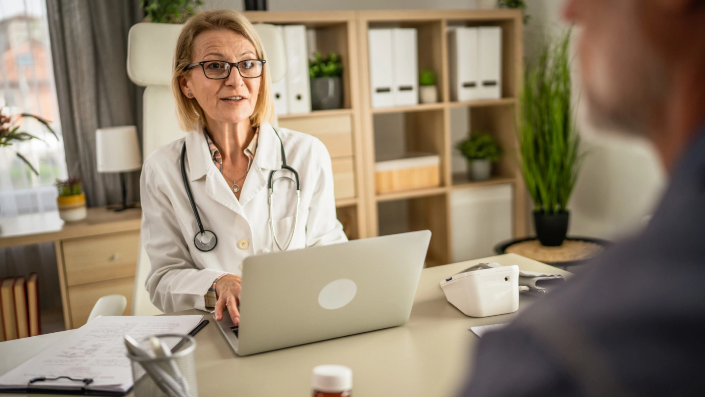 Eine Ärztin unterhält sich mit ihrem Patienten. Dabei tippt sie etwas am Computer.