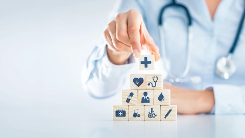 Человек со стетоскопом ставит друг на друга кубики с символами здоровья.