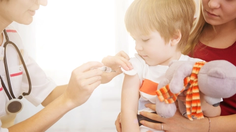 A child sitting on its mother’s lap being vaccinated in the upper arm.