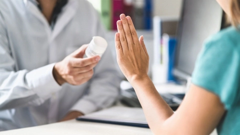 A doctor offering medication to a woman. She is holding up her hand to refuse it.