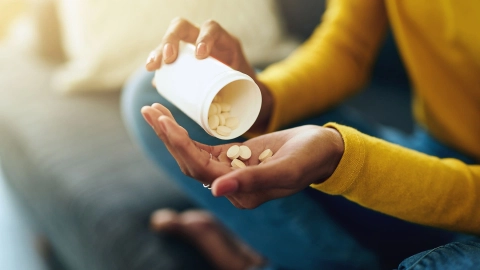 Nahaufname: Eine junge Frau schüttet mehrere Tabletten aus einer größeren Medikamentendose in ihre offene Hand.