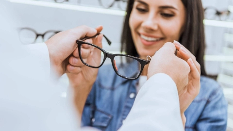 A young woman receives glasses from an optician