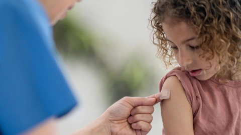 A nurse sticks a plaster onto a child’s upper arm.