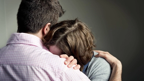 امرأة تُميل رأسها على كتف رجل. وتخفي وجهها في صدره. وتبدو يائسة.