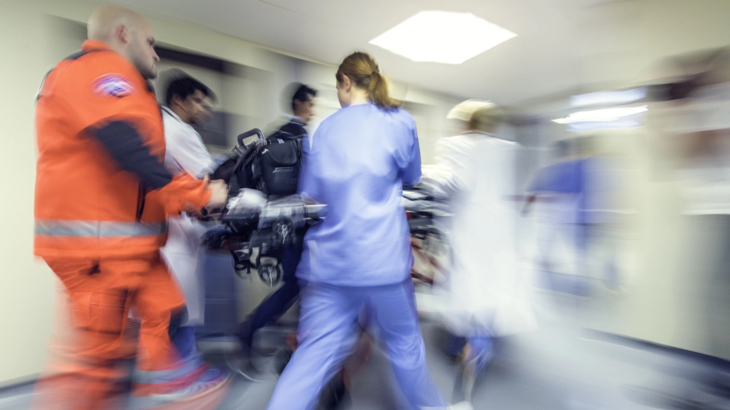 Notfallversorgung (Quelle: iStock/vm) Ein Notfallsanitäter, eine Krankenschwester und ein Notarzt schieben eine Trage mit einem Patienten durch einen Flur im Krankenhaus.