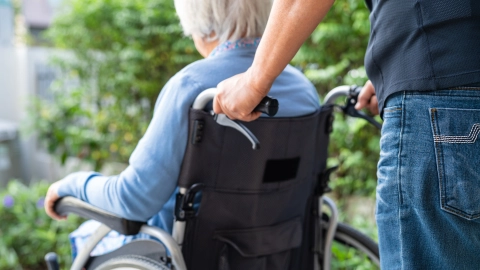 Yaşlı bir kadın tekerlekli sandalyede oturuyor ve bir adam tarafından itiliyor.