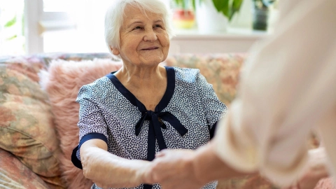 امرأة مسنة تحصل على مساعدة للوقوف من الأريكة.