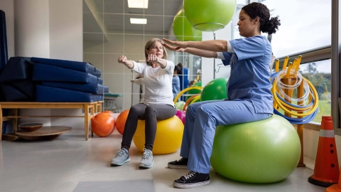 Woman does an exercise on a gym ball under the guidance of a physiotherapist.