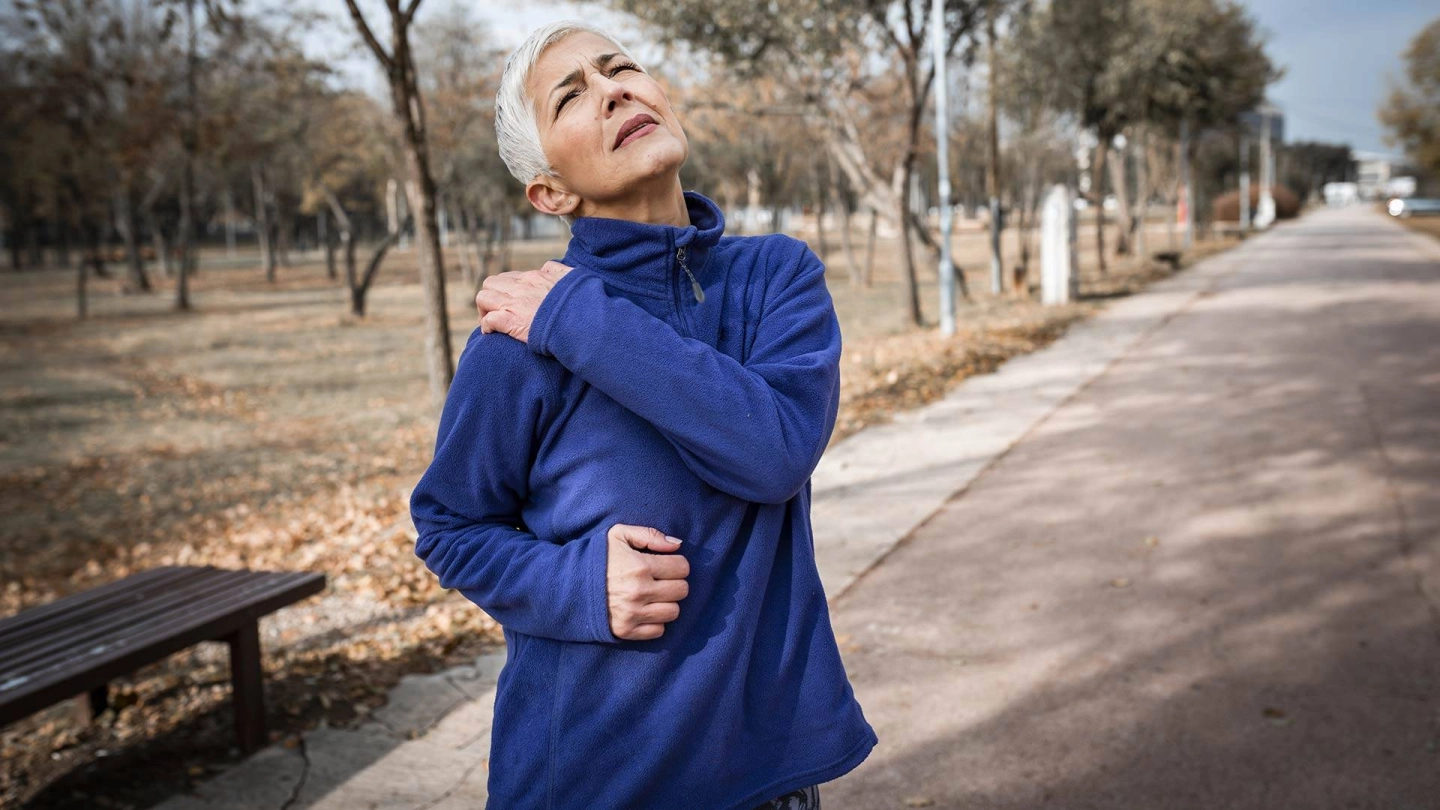 Rhabdomyolyse (Quelle: iStock/RealPeopleGroup) Eine Frau mit grauen Haaren beim Joggen: Sie greift sich mit der linken Hand an die rechte Schulter, die offenbar stark schmerzt.