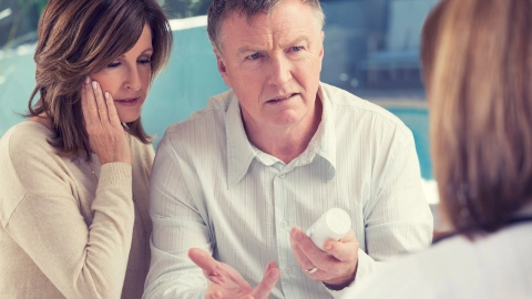 Complaining about medical treatment: a man and a woman are standing close together, a doctor is standing opposite them. The man is holding some medication in one hand. He is looking at the doctor in a questioning manner.
