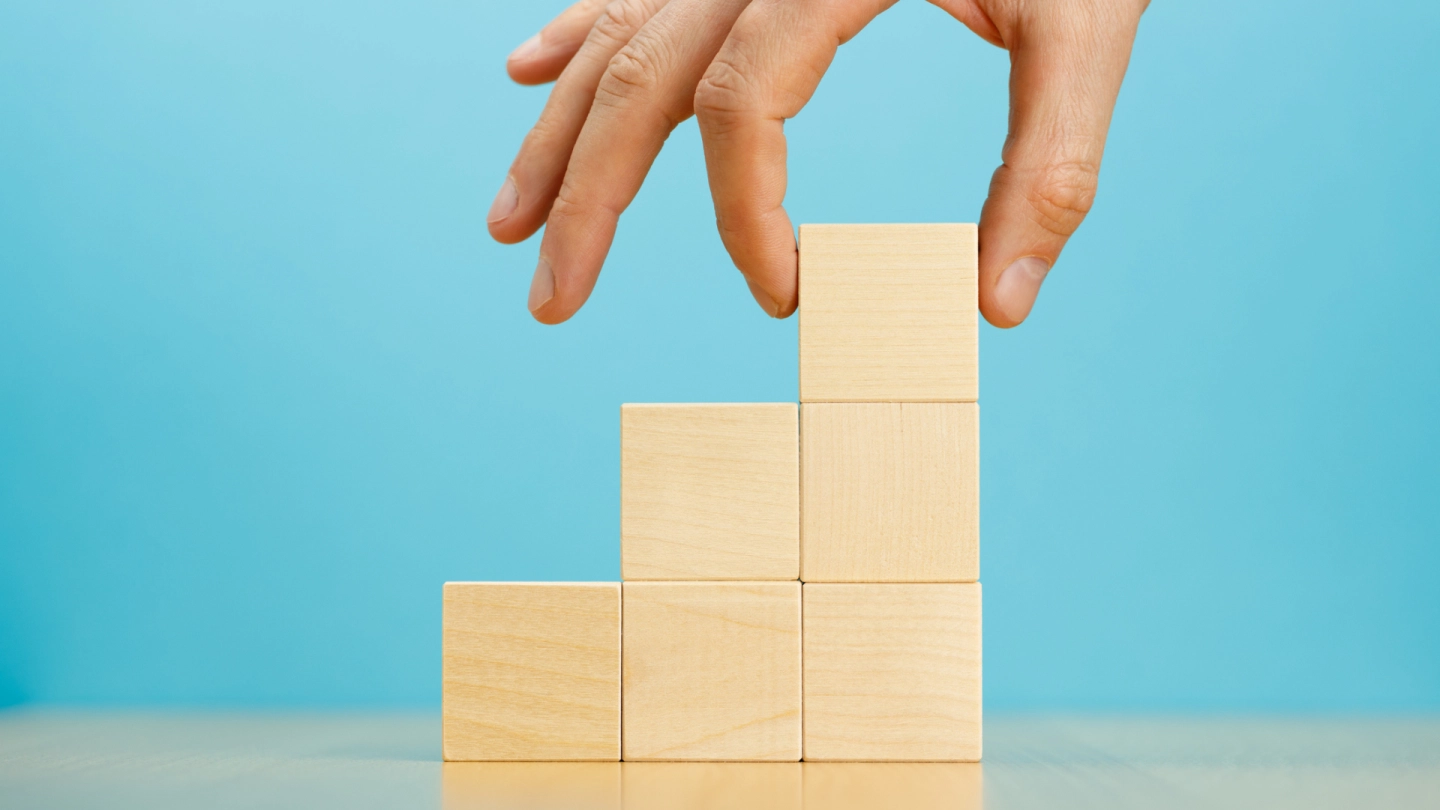 Eine Person setzt mit der Hand mehrere Würfel zu einer Treppe zusammen.