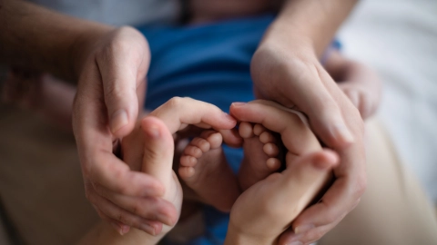 Die Hände der Eltern umschließen die Füße eines neugeborenen Kindes.